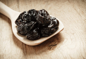 Prunes or dried plums on a wooden spoon - by Doug Cook RD
