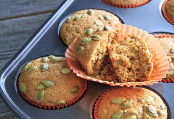 Homemade pumpkin muffins with single muffin sliced open sitting in muffin pan on rustic wooden table