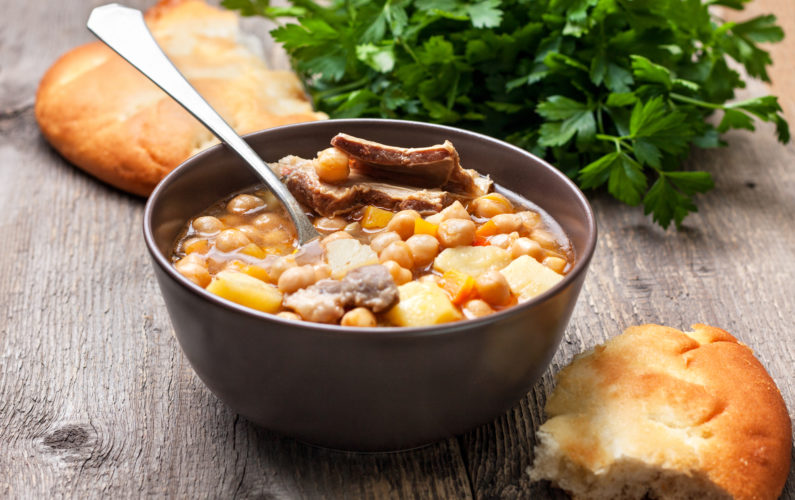 Moroccan harira soup with chickpeas and lamb, flat bread, parsley on a wooden background