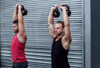 Two muscular men lifting a kettle bell