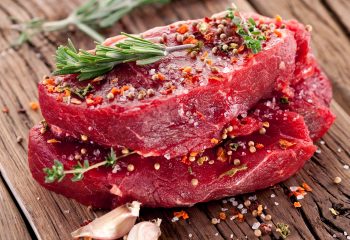 Raw beef steaks on a table top with sprig of rosemary and garlic